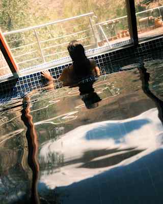 A woman in the Mayu Willka Spa spool stands at the edge gazing at views, in an eye-level view, seen from behind at an angle.