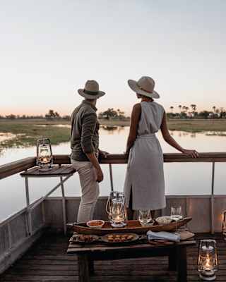 A couple standing on the bow of a candlelit boat at sunset in the Okavango Delta