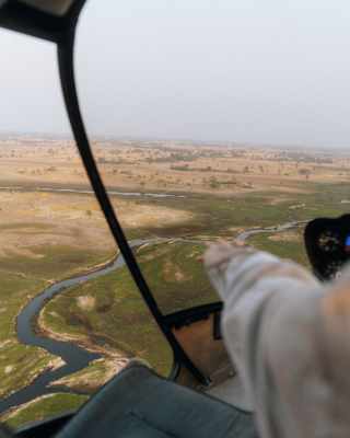 View through the window of a helicopter, looking down on the Okavango Delta's dry grasses that turn green close to the river.