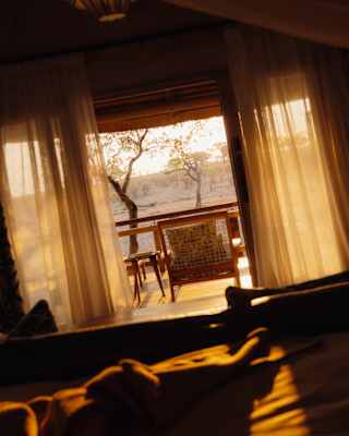 Angled image of a deck overlooking the plains, bathed in golden sun, seen through open drapes from a lodge interior.