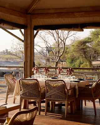 Soft sun illuminates a table with rope-back chairs awaiting diners on the covered deck of Savute Elephant Lodge restaurant.