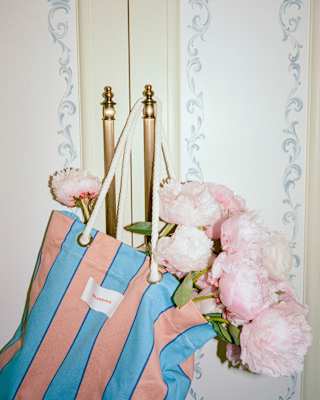 Stems of soft pink peonies fill a blue and pink-stripe tote bag which hangs from one of a pair of gold-tone cupboard handles.