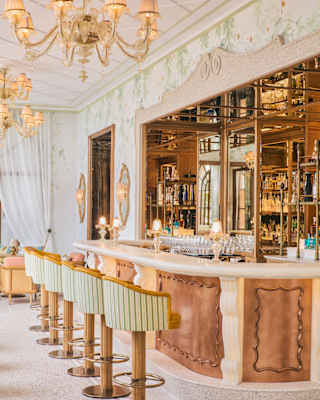 Six tub stools in mint and white stripe line a copper and marble bar in a view that captures a botanical wall mural surround.