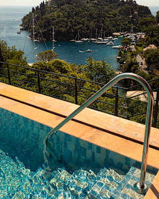 A hand rail at the corner of the pool descends into rippling waters in a view that captures the stunning Baia Cannone below.