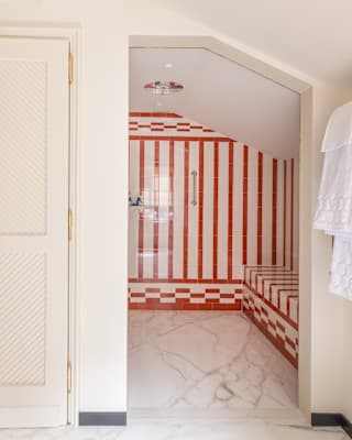 A white door opens to reveal a room with red and white striped tiled walls and a matching bench, with marble flooring and lace curtains on the right.