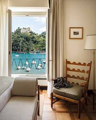 Suite interior with a chair and an open window with a view of boats on Portofino Bay