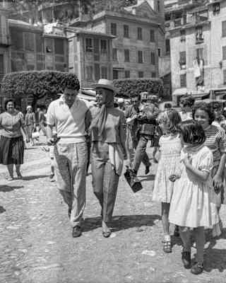 Liz Taylor walks arm-in-arm with Eddie Fisher, surrounded by locals, photographed by Francesco Leoni in black and white.