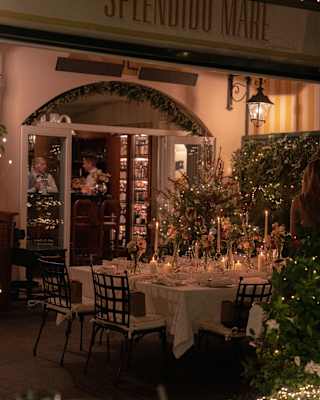 View of a dining room glowing and twinkling with festive decorations, with focus on a table filled with glasses and candles.