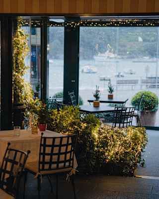 Warm-glow fairy lights adorn plant displays inside the dining room, with views through a large window out on to the marina.