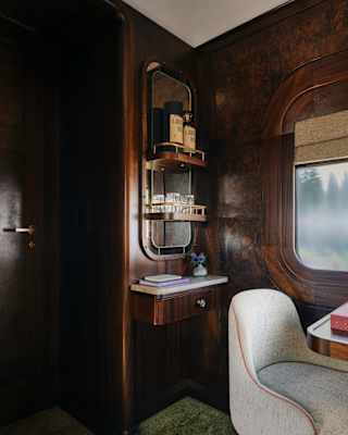 View into a cabin corner with mirrored wall shelves and a pale chair at a table by the window, which brings in natural light.