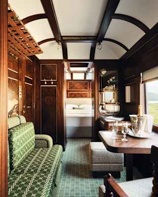 An emerald tweed banquette faces a window table where a Champagne cooler awaits, in a view through the Heron Grand Suite.