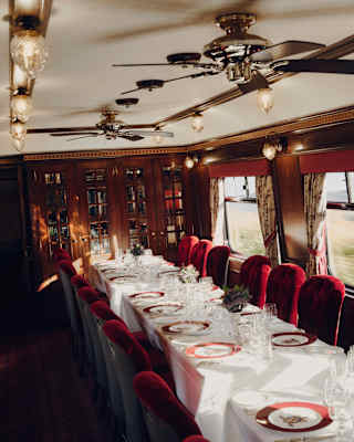 High-angle view over a row of three dining tables with red velvet chairs, laid with The Royal Scotsman branded plates.