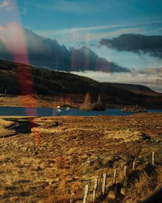 The train passes golden-grassed plains around a small lock, seen through a window that reflects hints of the interior.