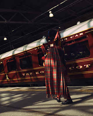 Half-hidden in shadow, a bagpipe player in traditional kilt, plays on a platform in front of the stationary train.