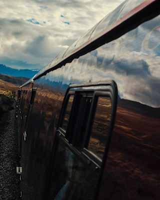 Close-up view down the exterior of the train, its carriages so glossy that they mirror the cloudy sky and the rugged highlands.