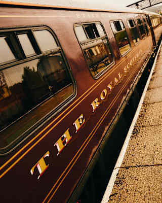 Tilted view of the the train exterior, with The Royal Scotsman in gold lettering on a maroon background, at a platform.
