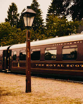 View of The Royal Scotsman's maroon carriages with gold lettering and white roof, seen past an old-fashioned street lamp.