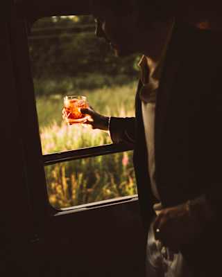 In the low-lit Observation Car, a man holds a tumbler of whisky which glows red as it catches a beam of sun by the window.