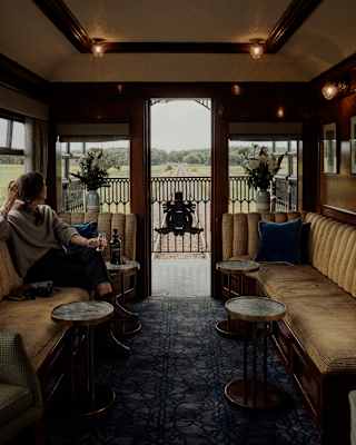 A woman relaxes with a drink on a banquette of warm gold upholstery as she gazes through the door of the observation deck.