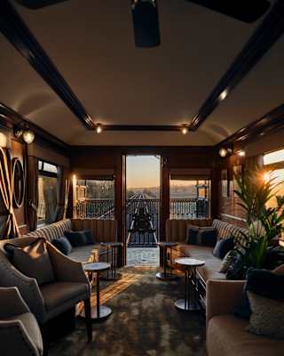 Tracks narrow with distance, seen beyond the Observation Car doors as sunset through windows stripes the low-lit interior.