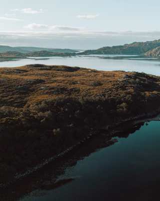 Still waters shimmer silvery-blue as they wrap around the heather-clad contours of a loch's banks in the Scottish Highlands.