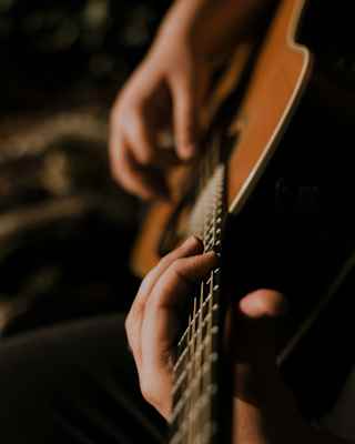 Close-up of a musician's hands as they play an acoustic guitar, seen from the fret end, in mellow light.