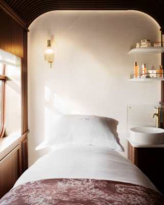 Inside a serene Dior Spa treatment room, with a fresh white bed, sink and shelves of products, cocooned in cedar panelling.