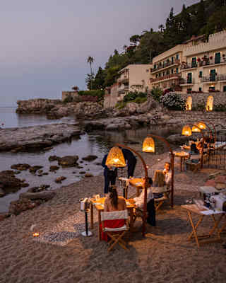 Diners are served on a private beach, their tables illuminated under private pools of light from tulip-shaped lamp stands