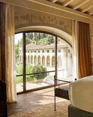 Glazed doors set into an arch bring views of the hotel into a calm bedroom with chinoiserie paper, cream décor and white bed.