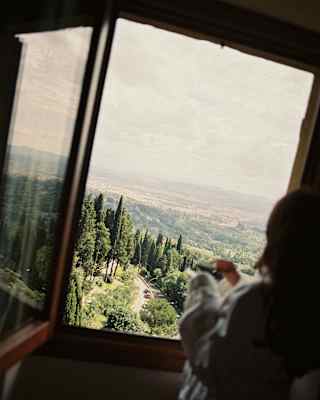 Angled shot of a guest in soft-focus as she gazes at the beautiful vista of Florence's hills and roofs from an upper window.