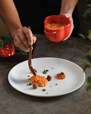 Chef Cozzolino spoons Carnaroli risotto with capsicum and sausage from a red bell-pepper-shaped dish on to a white plate.