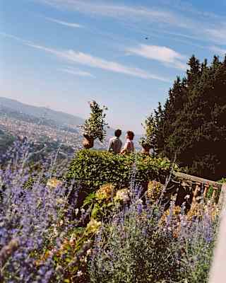 Angled image of two guests standing on the stone terrace in a garden bursting with lavender and foliage overlooking Florence.