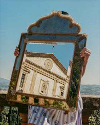 The pediment of Villa San Michele's front is reflected in a mirror which obscures the face of the person holding it, seen outside.