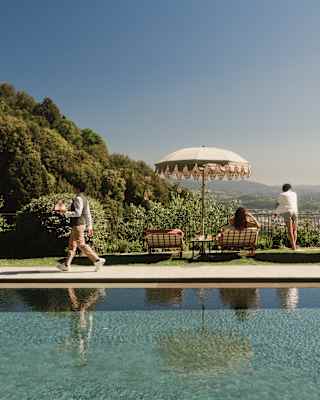 A waiter walks by the pool with a tray as a woman on a lounger and a man, standing close, face the other way to enjoy the views.