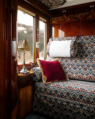 A large banquette in feather-pattern of blues and maroons and a plush red cushion catches light from the cabin window.