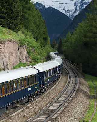 Gleaming blue and gold-detailed carriages snaking through a verdant valley