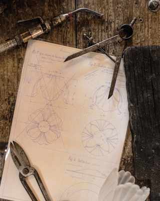 A fluted tulip of white blown glass, callipers and shears hold down artfully drawn plans for a cabbage-shape bowl