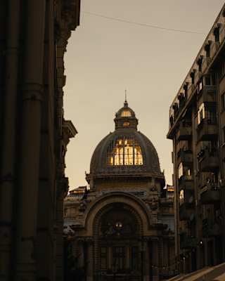 Evening light glows through the ornate glass lantern roof of Palatul CEC in Bucharest, seen from below at dusk.
