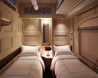 Two twin beds side-by side in a lamplit train cabin with light elegant decor