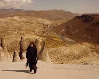 A woman with long dark hair and black clothes stands on a hill overlooking the Puruña stone forest and a valley river beyond.