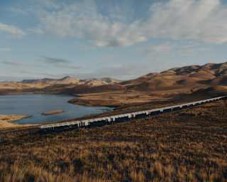 The train travels through russet grasslands overlooking the curves and contours of Lake Lagunillas, seen from a hill above.
