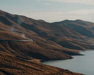 The Andean Explorer lets off steam as it cuts through the hill chain bordering Lake Lagunillas, grasses russet brown in sun.