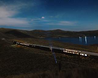 Night view of the Andean Explorer, lights in a few windows, as it travels through plains bordering a lake beneath the stars.