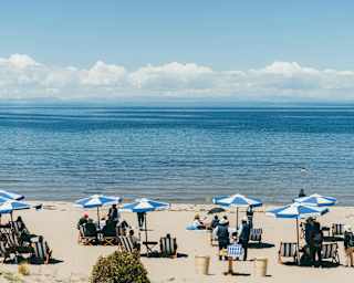 People relax on deck chairs beneath blue-striped parasols on the white sands of Collata Beach by Lake Titicaca's blue waters.
