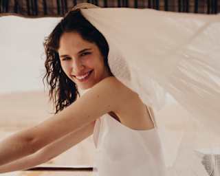 A dark-haired bride smiles to camera as she stands in a white dress on the Observation Car deck, veil billowing behind her.