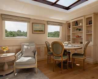 An armchair by a side table catches sunshine through two lounge windows, seen alongside a table with four dining chairs.