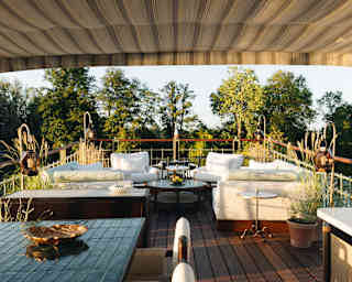 View across Coquelicot's luxurious deck with two white corner sofas and armchairs, a drinks table, lighting and plant pots.