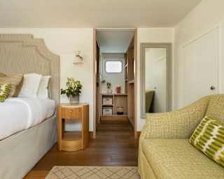 Eye-level view of a lower deck cabin with a bed, left, and green sofa, right, and a walkway through to a dressing room.