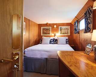 Lamplit wood-panelled barge cabin with a pillowy king-bed with navy blue accents