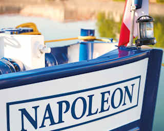 The pristine white side of a luxury barge with 'Napoleon' painted in blue lettering